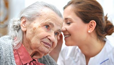 Eine Pflegerin flüstert der Seniorin etwas ins Ohr
