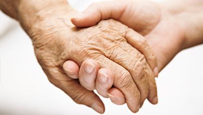 Zwei Hände halten sich fest, eine Hand von einer/einem Senior*in, die anderen von einer jüngeren Person