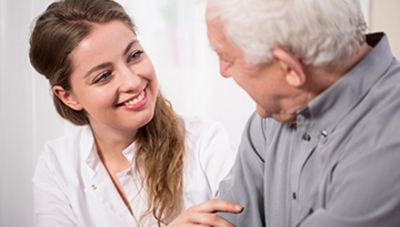 Eine Pflegerin spricht mit einem Senior, ihre Hand ist auf seinem Arm