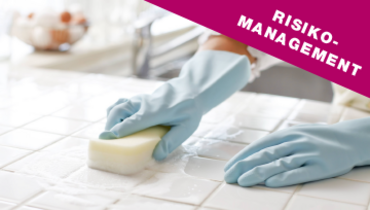 Eine Reinigungskraft putzt mit Handschuhen eine Arbeitsfläche – im Blickfang steht "Risikomanagement"