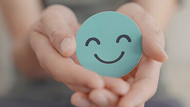 Zwei Hände halten einen grünen und lächelnden Smiley